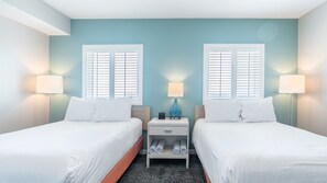 Ein Hotelzimmer mit zwei Betten, einem Nachttisch mit Lampe und einem kleinen Regal mit zusammengerollten Handtüchern.
