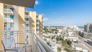 Ein Balkon mit einem Stuhl, der auf einen Wohnbereich mit mehrstöckigen Gebäuden und ungehindertem Blick auf den Strand blickt.