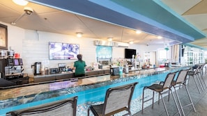 A bar area with a long counter, bar stools, a coffee machine, and a television screen. - North Myrtle Beach | Oceanfront Family Stay | Pool & Beach | 3BR Sleeps 10 (North Myrtle Beach)