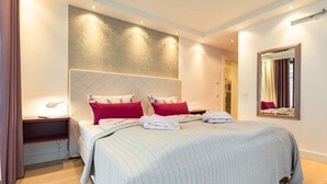 Habitación de hotel con una cama grande, dos mesitas de noche, un espejo y una lámpara fijada a la pared.