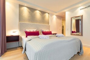 Een hotelkamer met een groot bed, twee nachtkastjes, een spiegel en een wandlamp.