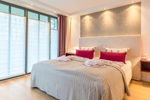 Ein Hotelzimmer mit einem großen Bett, einem Kopfteil mit strukturierter Musterung und Blick durch raumhohe Fenster.
