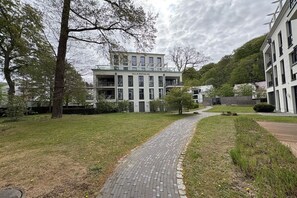 Een pad dat leidt naar een modern gebouw met een naamplaatje, omringd door groen en bomen.