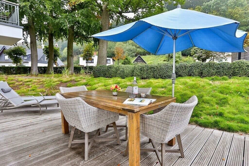 Un espace extérieur aménagé pour les repas, avec une table en bois et des chaises en osier, un parasol bleu et une terrasse.
