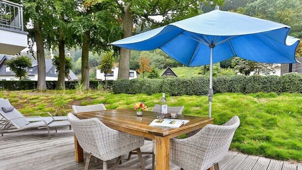 Un área de comedor al aire libre con una mesa de madera, sillas de mimbre, un paraguas azul y una terraza.