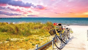 Una playa con un camino de madera, bicicletas y un muelle al fondo.