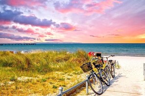 Een strand met een houten looppad, fietsen en een pier op de achtergrond.