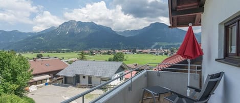 A balcony with a view of mountains, a red umbrella, and a table with chairs.