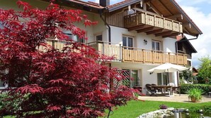 A two-story building with a balcony, a dining area with outdoor furniture, and a small pond. - Holiday apartment with 1 bedroom (Seebruck)
