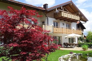 Un edificio a due piani con un balcone, una zona pranzo con arredi da esterno e un piccolo stagno.