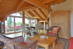 Ein geräumiges Zimmer mit Holzbalkendecke, einem Essbereich mit Stühlen und Tisch sowie einer großen Schrankwand.