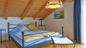 A bedroom with a wooden ceiling, a bed with a metal frame, a bedside lamp, and a view of the outdoors. - Holiday apartment with 1 bedroom (Seebruck)