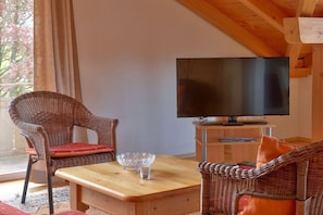 Ein möblierter Raum mit Fernseher, Korbstühlen, einem Holztisch und einer Glasvase.