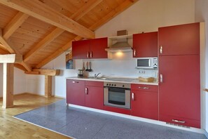 Eine Küche mit roten Schränken, einem Edelstahlbackofen und einer Mikrowelle.