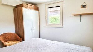 Ein Schlafzimmer mit einem Bett, einem Kleiderschrank, einem Korbstuhl, einem Fenster und einem Regal.