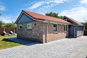 A single-story brick house with a red-tiled roof, a covered patio area, and a fenced backyard with two lounge chairs. - Holiday apartment OK16 Oostkapelle (Oostkapelle)