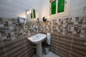 Une salle de bain avec un lavabo blanc, un sèche-cheveux, un miroir et une fenêtre verte.