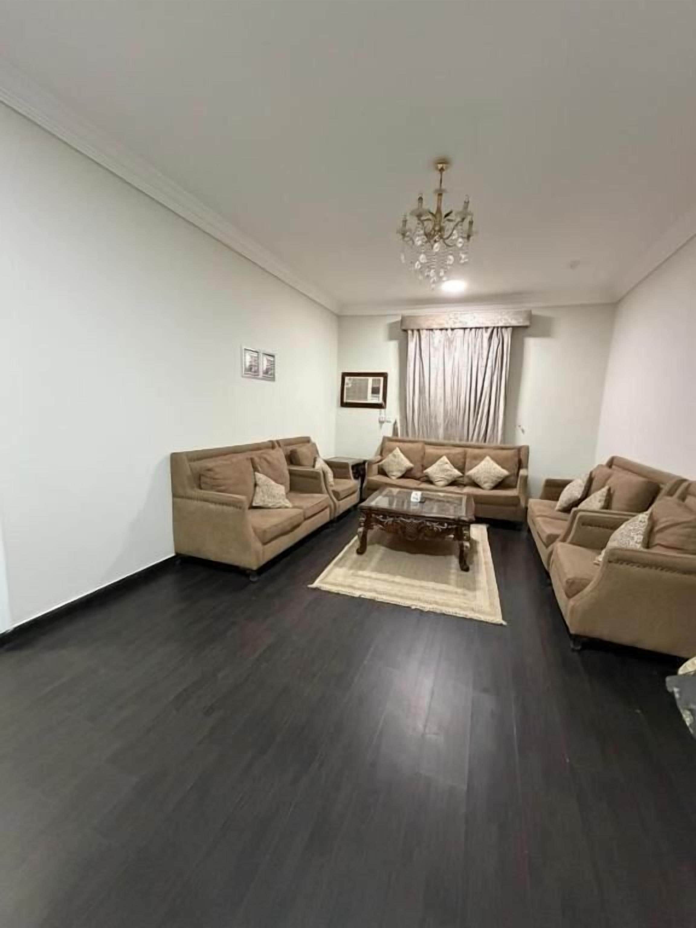 A living room with a dark wood floor, beige sofas, a coffee table, and a chandelier.