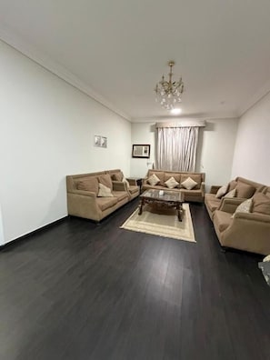 A living room with a dark wood floor, beige sofas, a coffee table, and a chandelier.
