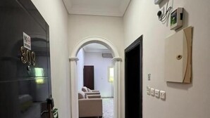Un pasillo con piso estampado, una puerta con señal de número y un cuadro de luz fijado a la pared.