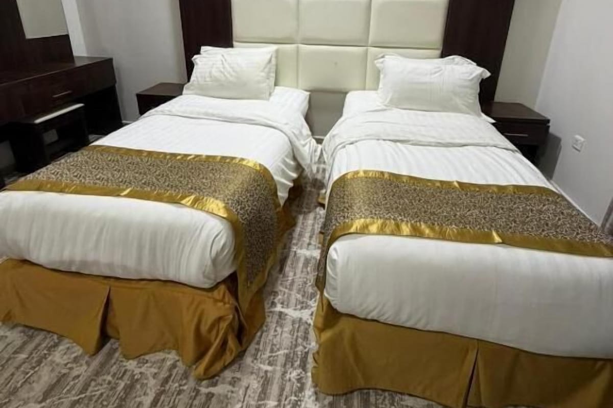 Une chambre d’hôtel avec deux lits, une grande tête de lit rembourrée et une table de chevet en bois.