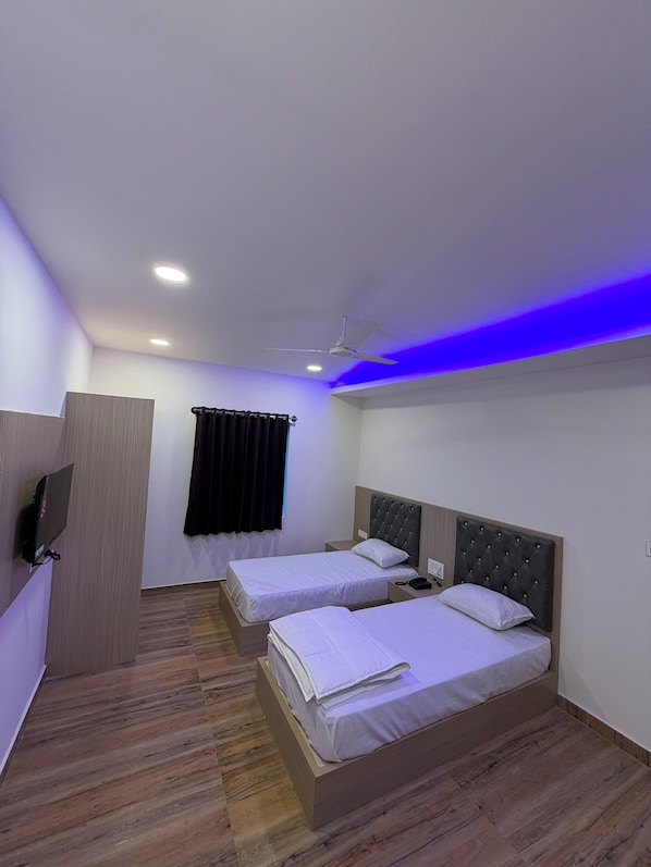 Habitación de hotel con dos camas, un ventilador de techo y un televisor montado en la pared.