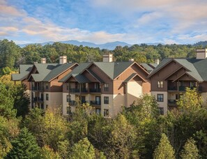 A multi-story hotel with a modern architectural design, featuring balconies and a view of the surrounding forest and mountains. - Sevierville | Pool & Mountains | Nature Escape Stay (Sevierville)