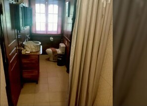 Un baño con lavamanos, inodoro y ventana con persianas.