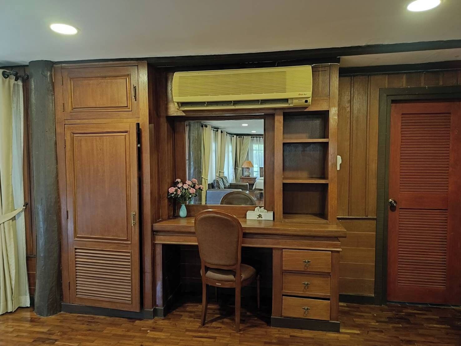 A wooden desk with a chair, a mirror, and a vase with flowers.