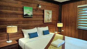 Quarto de hotel com parede revestida de madeira, cama com roupa de cama branca e azul, duas luminárias de cabeceira e obras de arte.
