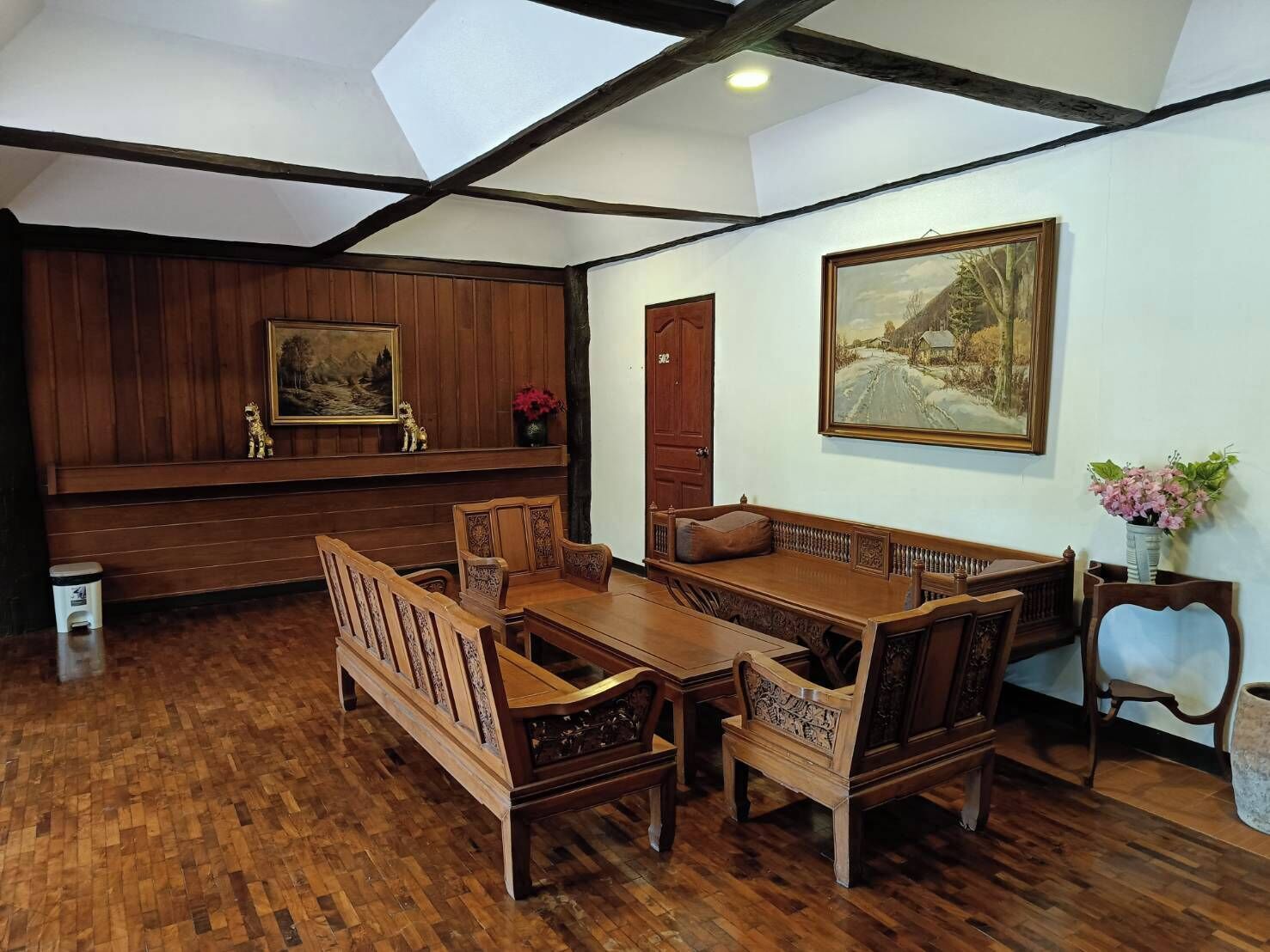 A room with a wooden dining set, a bench, and two paintings on the walls.