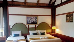 A hotel room with two beds, wooden beams on the ceiling, a painting on the wall, and a nightstand with a lamp.