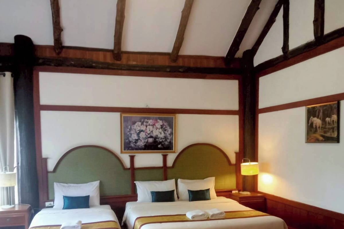 Habitación de hotel con dos camas, vigas de madera en el techo, un cuadro en la pared y una mesita de noche con una lámpara.