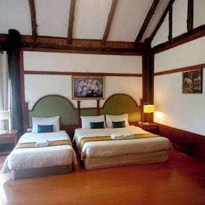 Habitación de hotel con dos camas, vigas de madera en el techo, un cuadro en la pared y una mesita de noche con una lámpara.