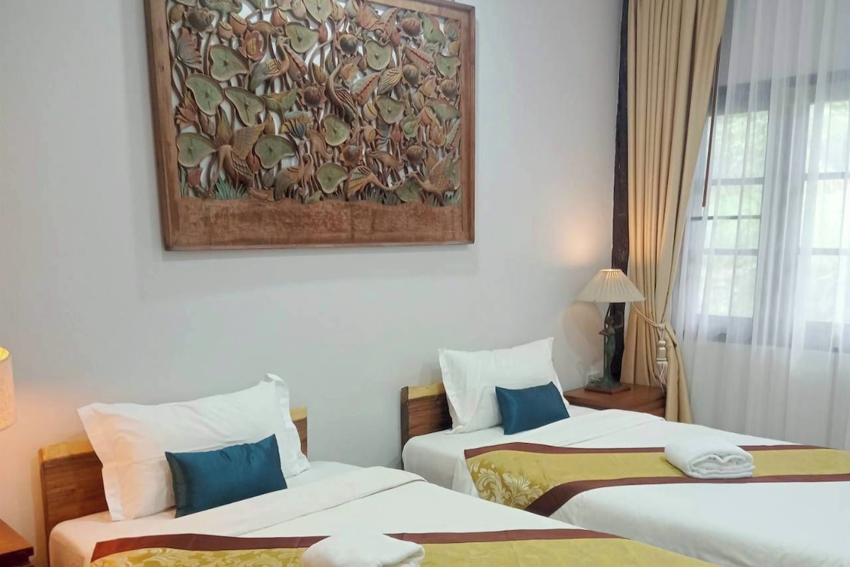 A hotel room with two beds, a decorative wall piece, a window with curtains, and a bedside lamp.