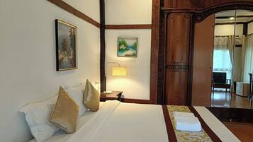 A hotel room with a large bed, a wooden door, a painting on the wall, and a lamp.