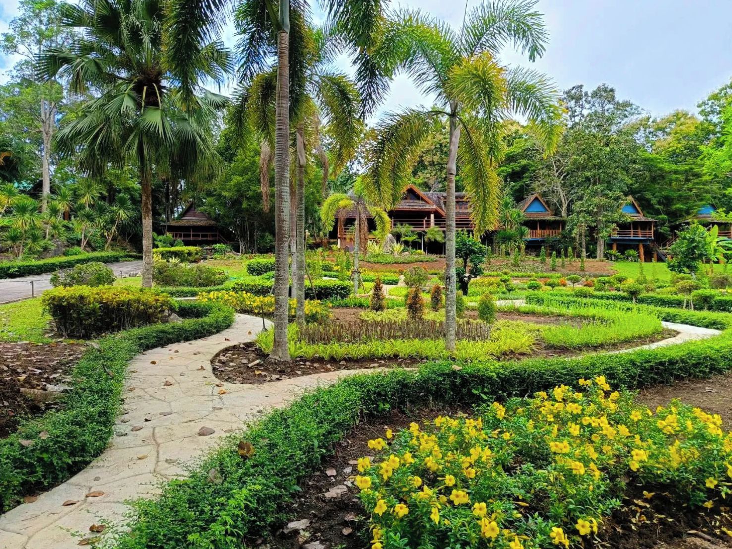A tropical resort with a well-maintained garden, palm trees, and traditional-style villas.