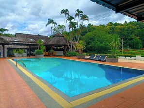 Una piscina con solárium empinado, sillas de descanso y plantas tropicales.