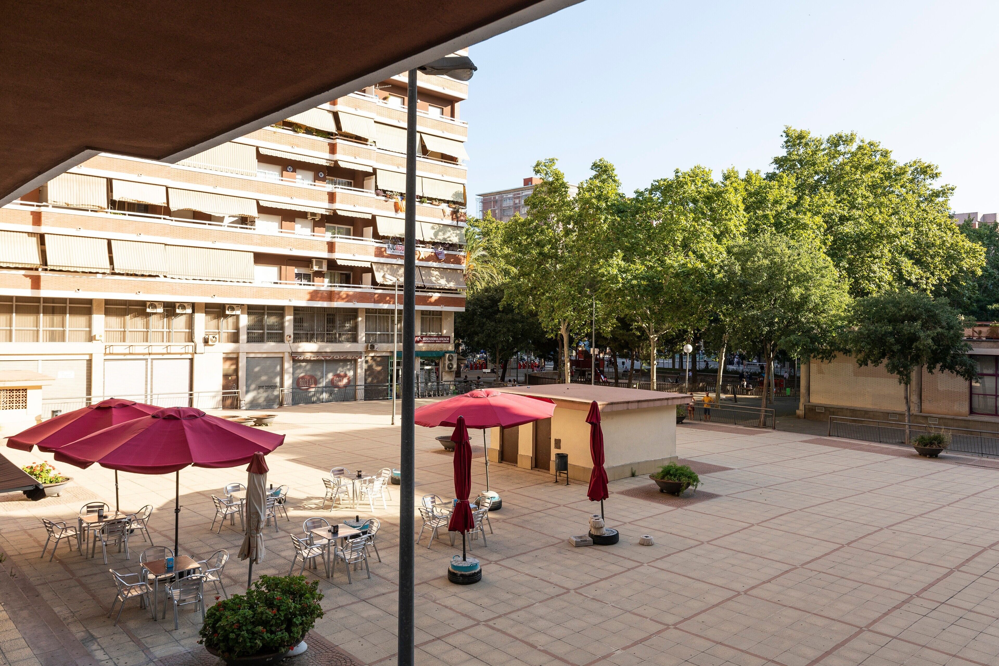 A courtyard with outdoor seating, a building with balconies, and a large tree.