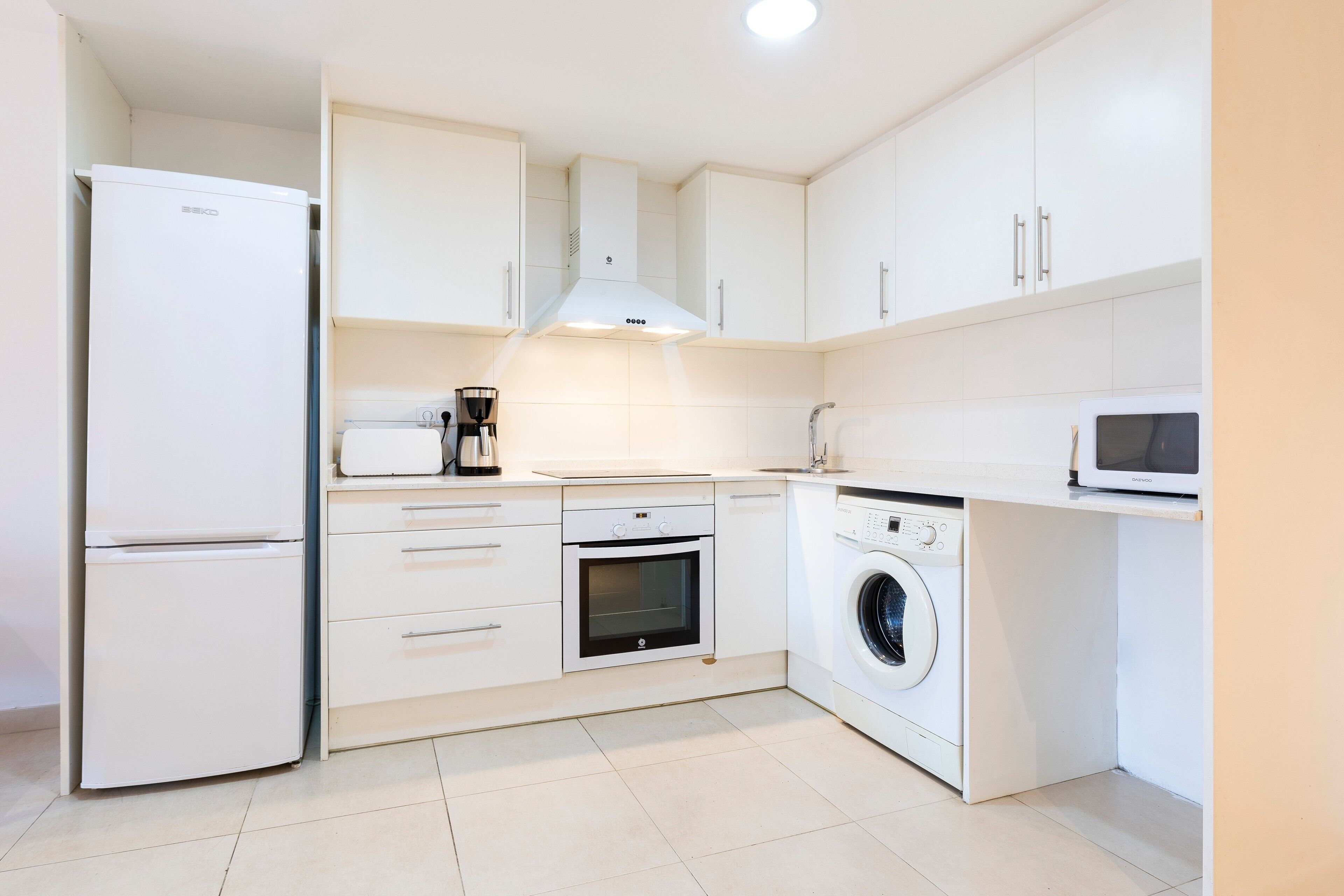 Une cuisine compacte équipée d’un réfrigérateur, d’un four, d’un four à micro-ondes et d’un lave-linge.