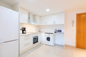 Een kleine keuken met een koelkast, oven, magnetron en wasmachine.