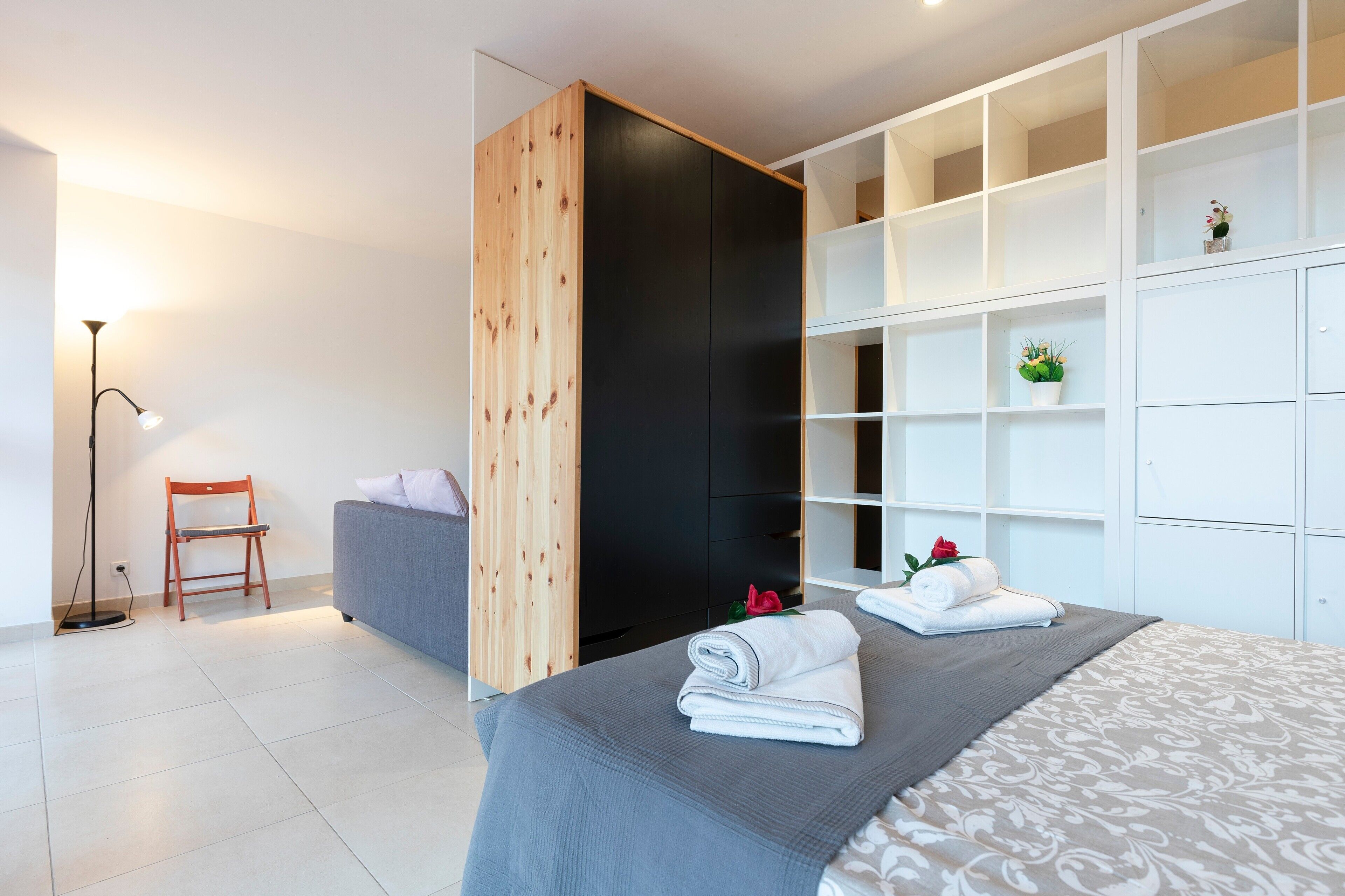 A modern bedroom with a bed, a grey sofa, a wooden wardrobe, and a floor lamp.