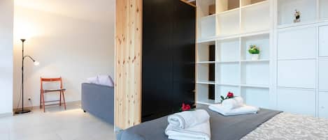 A modern bedroom with a bed, a grey sofa, a wooden wardrobe, and a floor lamp.