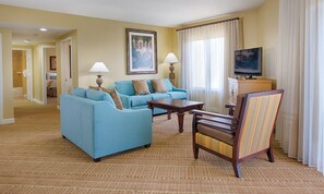 A hotel room with a blue sofa set, a wooden chair, a small table, a TV, and a painting on the wall. - Orlando | Pool & Disney Access | 3BR Sleeps 10 (Lake Buena Vista)
