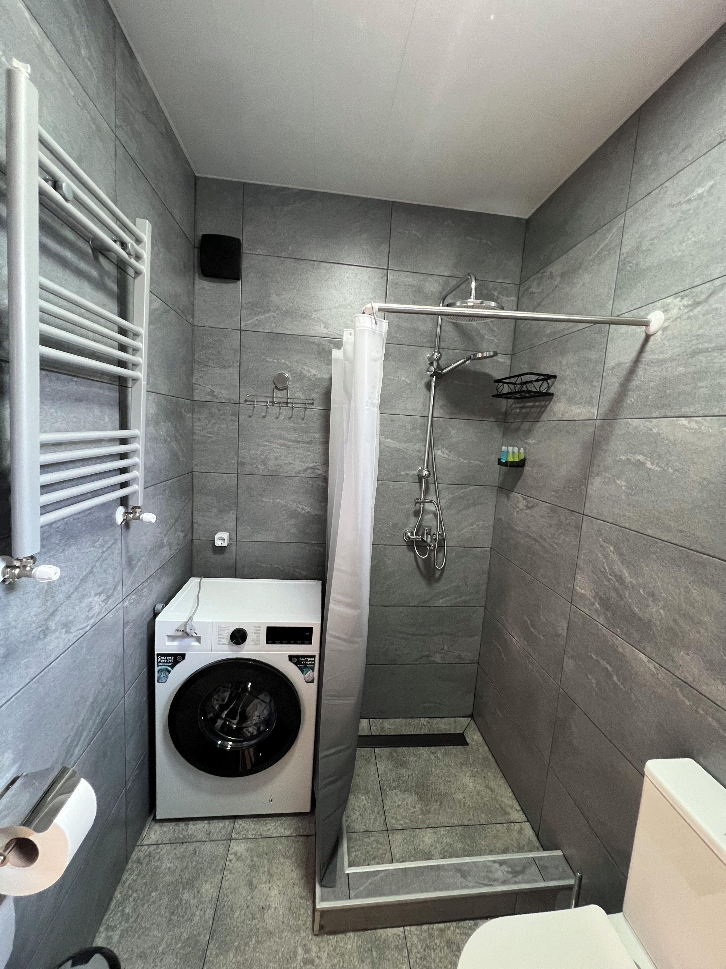 A compact bathroom with a washing machine, a shower with a glass door, and a towel rack.