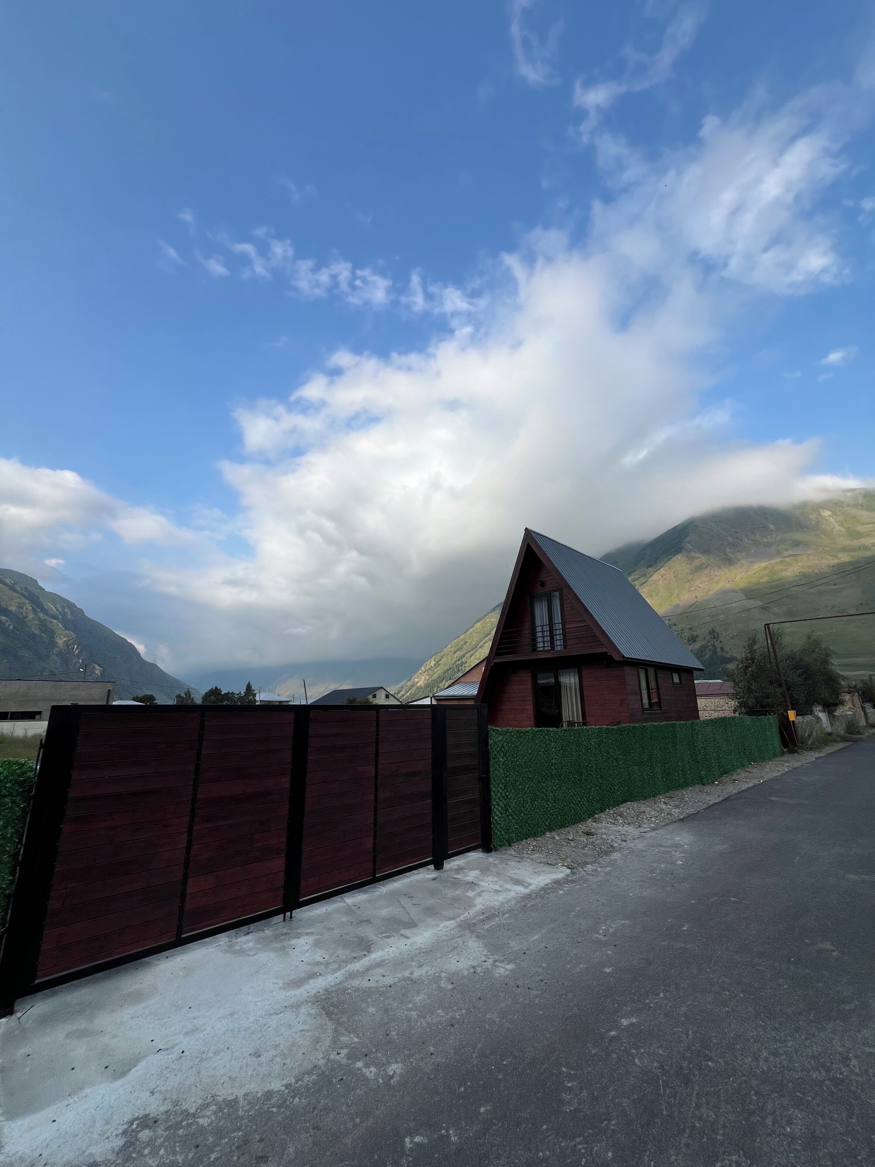 A house with a sloped roof, a fenced yard, and a road in the foreground.