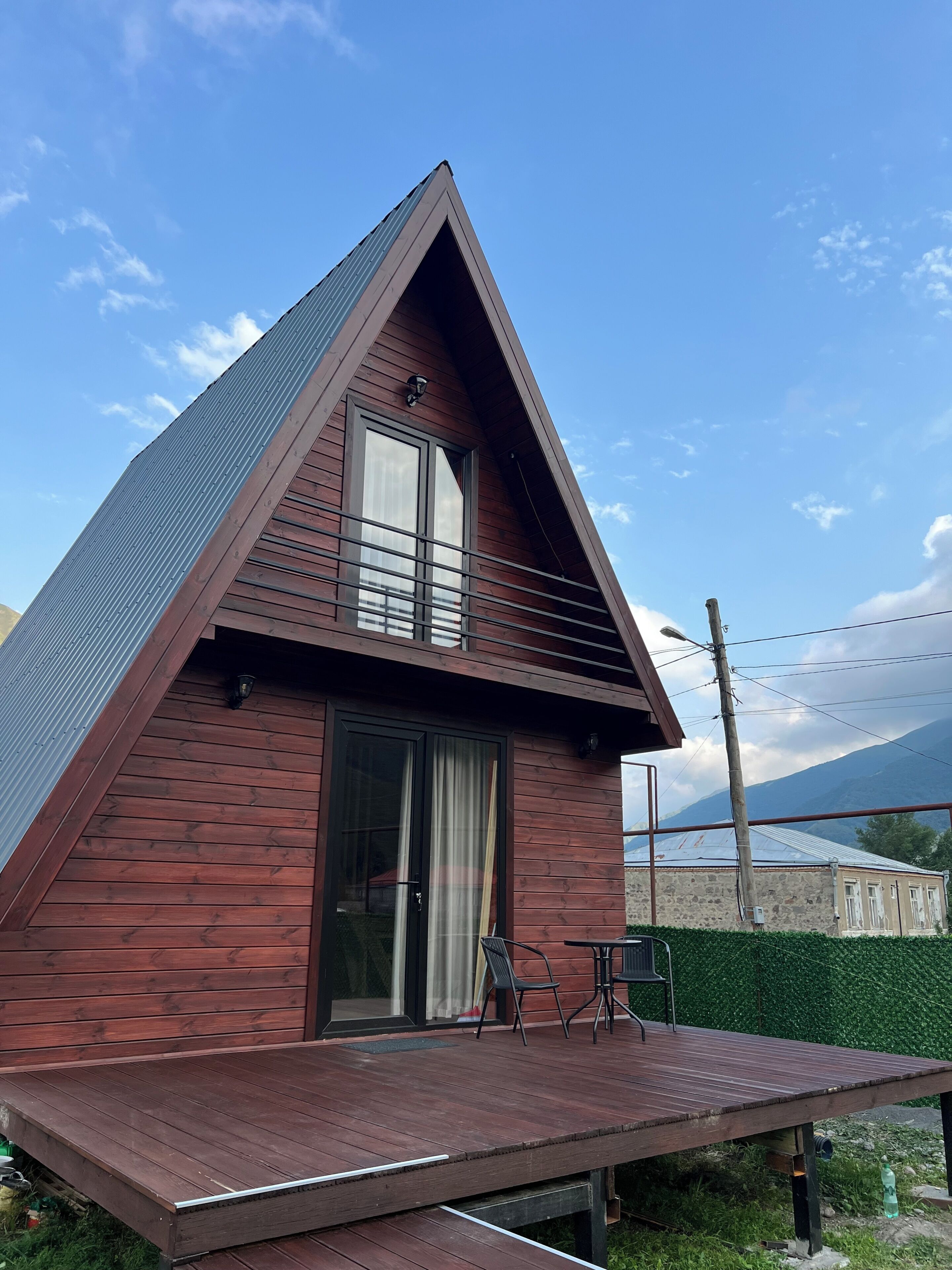 A triangular wooden house with a glass door and a small deck.