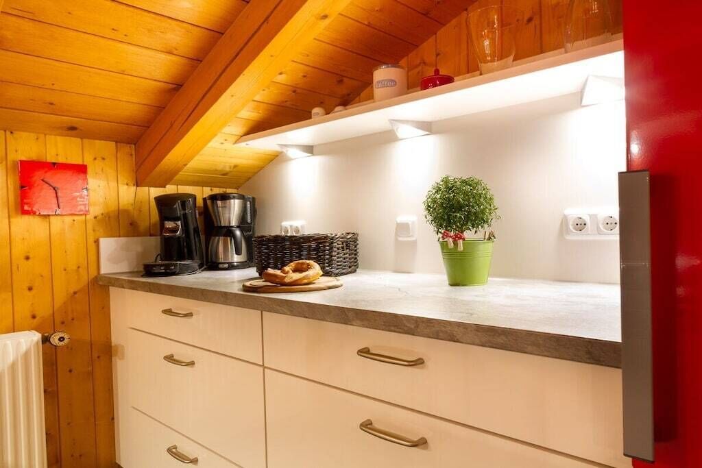 A kitchen with wooden cabinets, a coffee maker, a basket, a plant, and a red refrigerator.