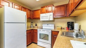Una cocina con armarios de madera, un refrigerador blanco, un microondas, una estufa y un lavamanos.