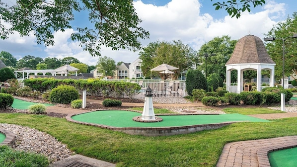 Un campo de mini golf con un pabellón, césped impecable y un cielo despejado.